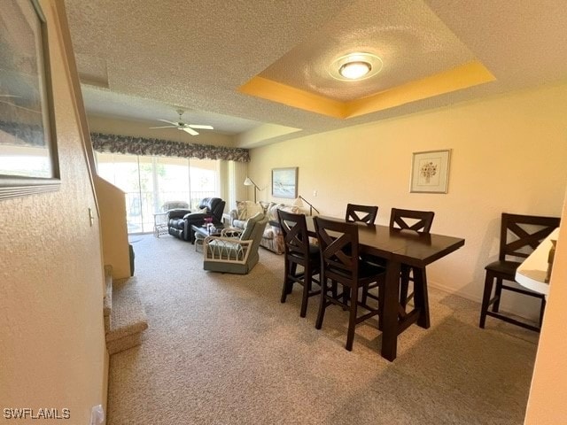 dining area with a textured ceiling, carpet floors, a tray ceiling, and ceiling fan