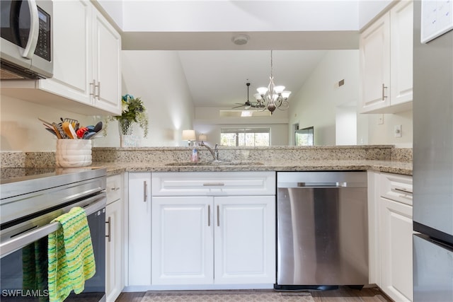 kitchen featuring white cabinets, stainless steel appliances, vaulted ceiling, and light stone countertops