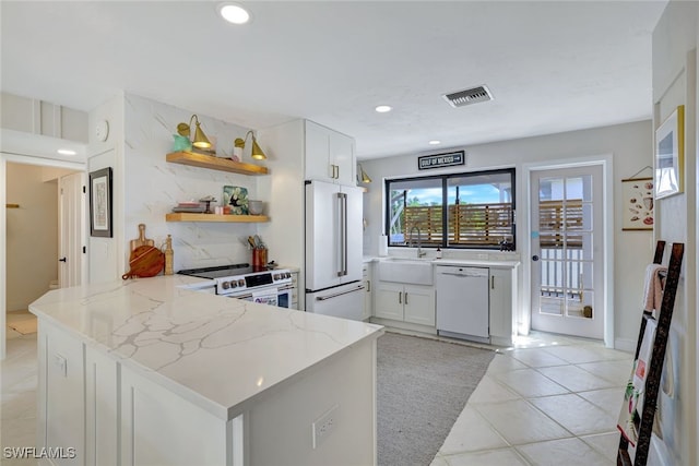 kitchen featuring white cabinetry, sink, light stone counters, kitchen peninsula, and white appliances