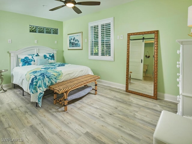 bedroom featuring a barn door, ceiling fan, and light wood-type flooring