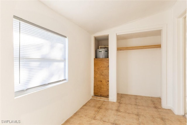 unfurnished bedroom featuring multiple windows, a closet, light tile patterned floors, and vaulted ceiling