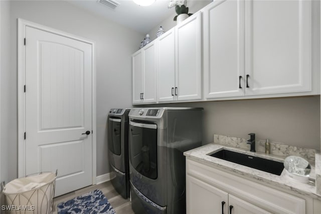 laundry area featuring washer and clothes dryer, sink, cabinets, and light hardwood / wood-style floors