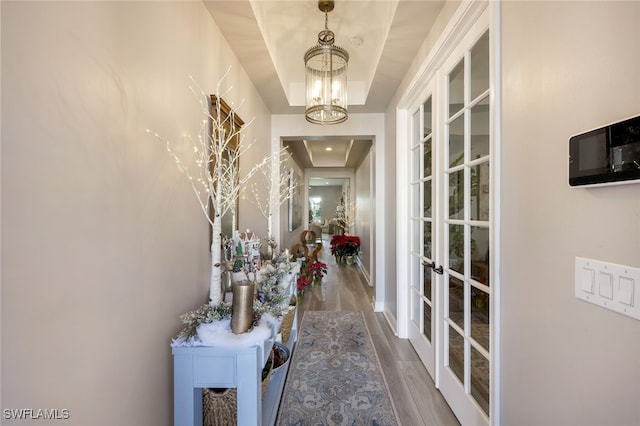 corridor featuring french doors, hardwood / wood-style flooring, a raised ceiling, and a notable chandelier