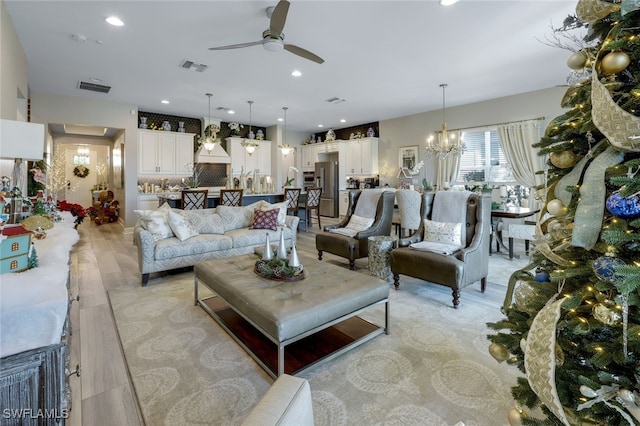 living room featuring ceiling fan with notable chandelier and light wood-type flooring