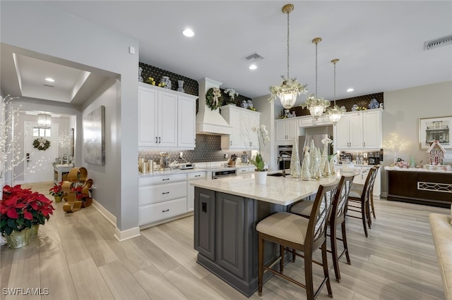 kitchen featuring pendant lighting, light stone counters, white cabinetry, and an island with sink