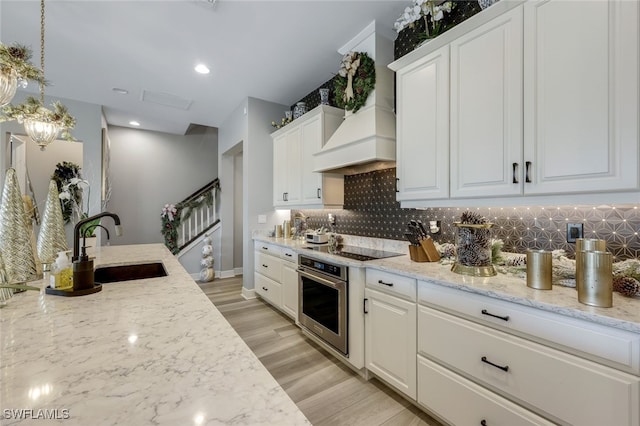 kitchen with tasteful backsplash, stainless steel oven, custom range hood, sink, and white cabinets