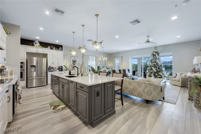 kitchen with white cabinets, stainless steel refrigerator with ice dispenser, ceiling fan with notable chandelier, and hanging light fixtures