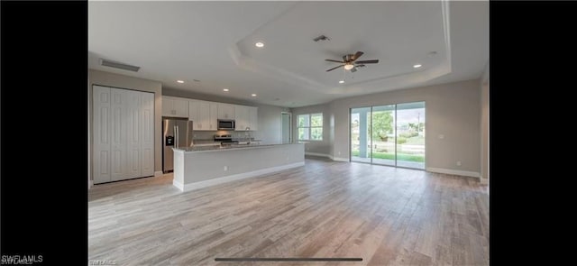 unfurnished living room with light wood-type flooring, a tray ceiling, and ceiling fan