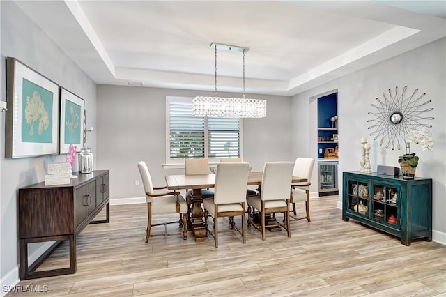 dining area featuring a notable chandelier, light hardwood / wood-style flooring, beverage cooler, and a tray ceiling