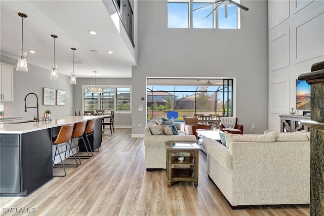 living area with recessed lighting, light wood-type flooring, a towering ceiling, and baseboards