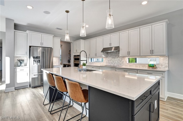 kitchen with a kitchen island with sink, hanging light fixtures, stainless steel refrigerator with ice dispenser, light hardwood / wood-style floors, and white cabinetry