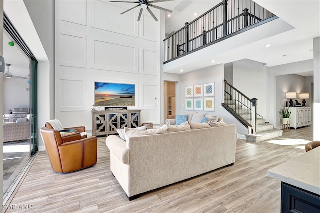 living room with a towering ceiling, light wood-type flooring, and ceiling fan