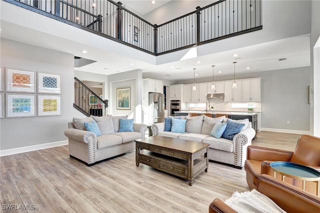 living room with baseboards, a towering ceiling, light wood-style flooring, stairway, and recessed lighting