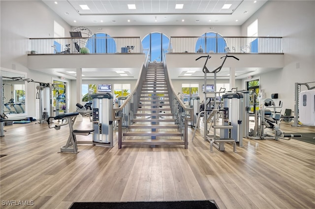 workout area with light wood-style floors and a towering ceiling