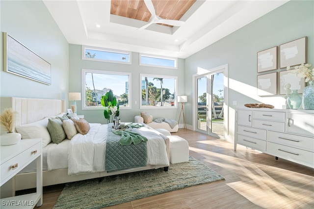 bedroom with a tray ceiling, hardwood / wood-style floors, a high ceiling, and access to outside