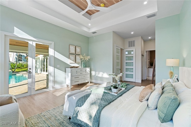 bedroom featuring a raised ceiling, access to exterior, hardwood / wood-style flooring, and french doors