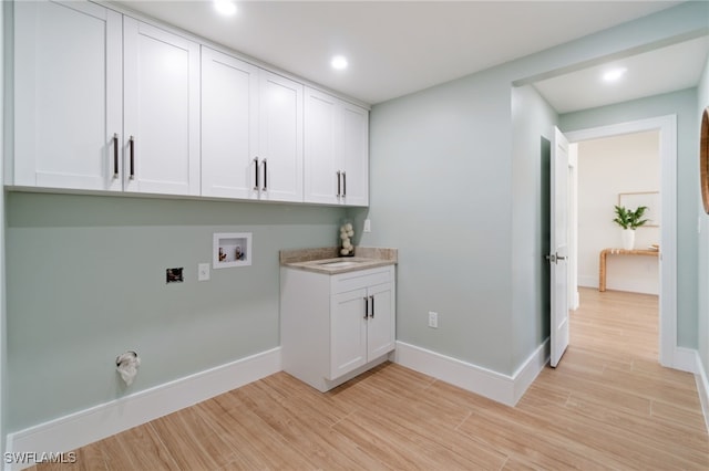 laundry area featuring washer hookup, light hardwood / wood-style floors, and cabinets