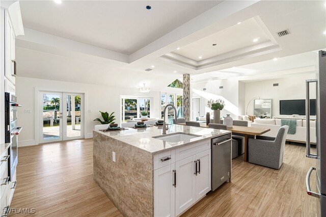 kitchen featuring white cabinets, sink, light hardwood / wood-style flooring, light stone countertops, and an island with sink