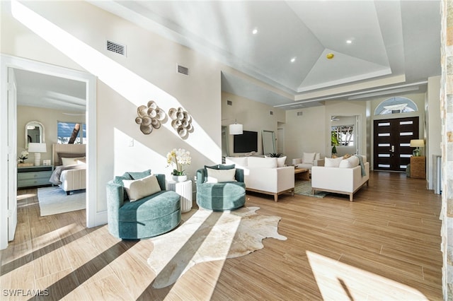 living room with a tray ceiling, high vaulted ceiling, and wood-type flooring