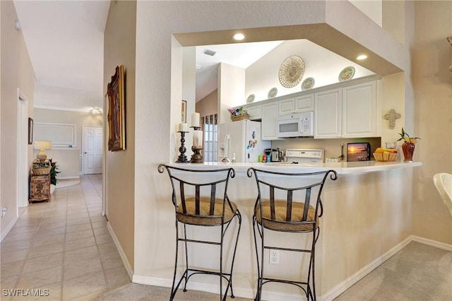 kitchen with a breakfast bar area, white cabinets, light tile patterned floors, kitchen peninsula, and white appliances