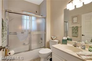 full bathroom with bath / shower combo with glass door, vanity, and toilet