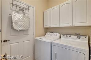 clothes washing area with separate washer and dryer and cabinets