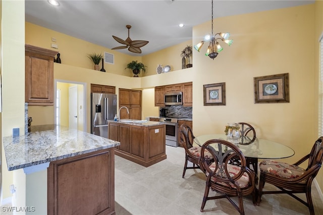 kitchen featuring kitchen peninsula, appliances with stainless steel finishes, light stone countertops, a towering ceiling, and a center island