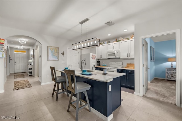 kitchen with pendant lighting, a breakfast bar, white appliances, an island with sink, and white cabinetry