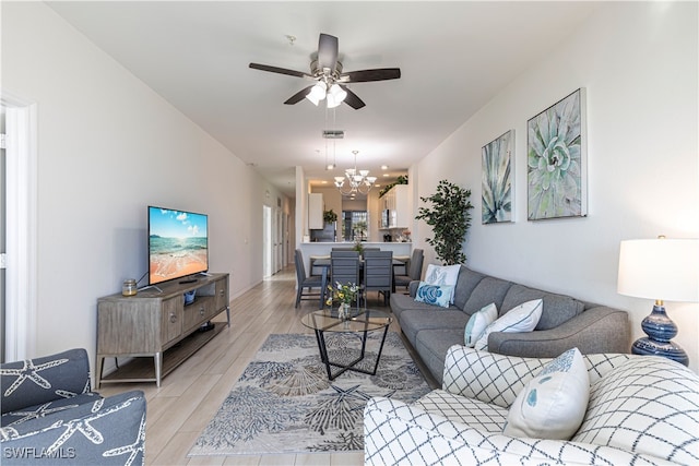 living room featuring ceiling fan with notable chandelier and light wood-type flooring