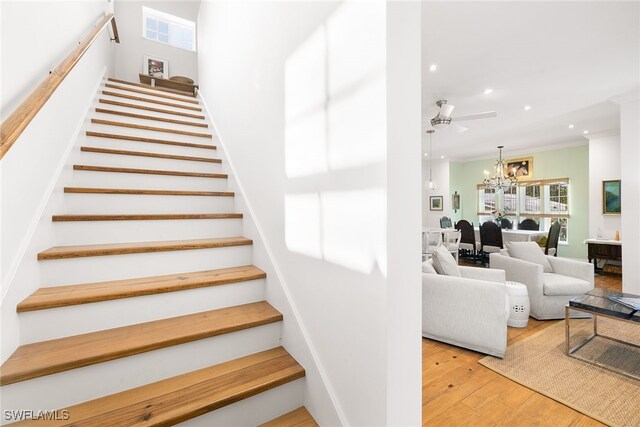 stairway featuring ornamental molding, ceiling fan with notable chandelier, and hardwood / wood-style flooring