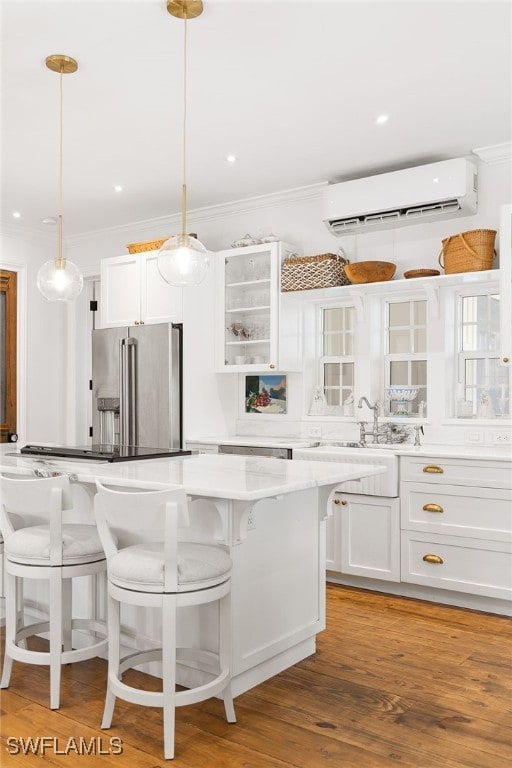 kitchen featuring a wall mounted air conditioner, high end fridge, pendant lighting, white cabinets, and light hardwood / wood-style floors