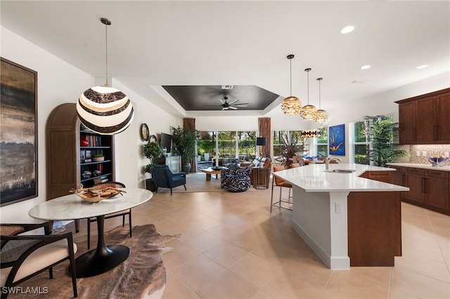 kitchen with sink, a tray ceiling, an island with sink, a kitchen bar, and decorative light fixtures