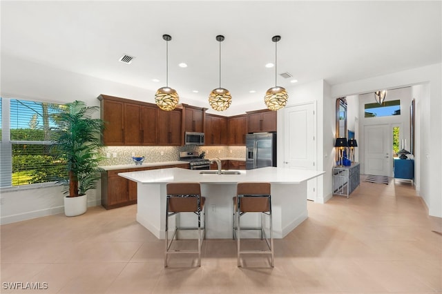 kitchen featuring sink, appliances with stainless steel finishes, hanging light fixtures, tasteful backsplash, and a center island with sink