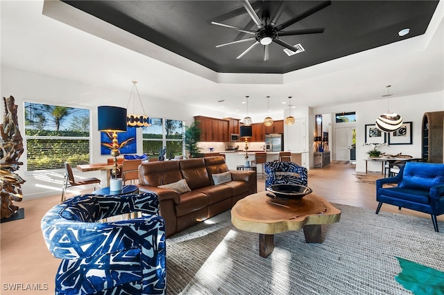 tiled living room featuring a raised ceiling and ceiling fan with notable chandelier