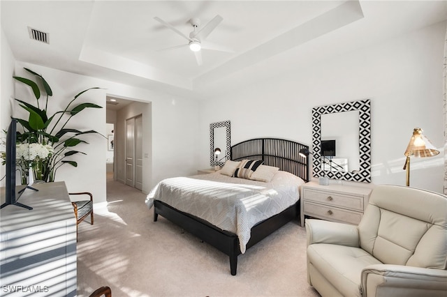 carpeted bedroom featuring ceiling fan, a raised ceiling, and a closet