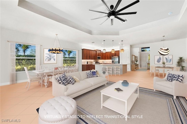 tiled living room with ceiling fan with notable chandelier, a raised ceiling, and a healthy amount of sunlight