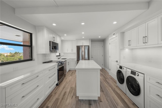 kitchen with decorative backsplash, independent washer and dryer, a kitchen island, white cabinetry, and stainless steel appliances