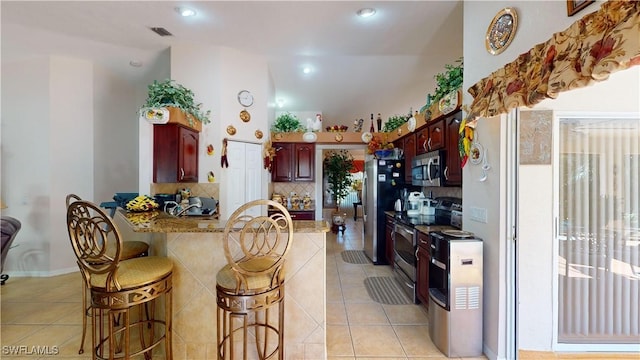 kitchen with kitchen peninsula, a kitchen breakfast bar, light stone counters, stainless steel appliances, and light tile patterned flooring