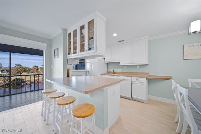 kitchen featuring ornamental molding, white appliances, light hardwood / wood-style floors, white cabinetry, and a breakfast bar area