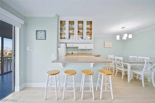 kitchen featuring a breakfast bar, crown molding, white refrigerator, decorative light fixtures, and white cabinets