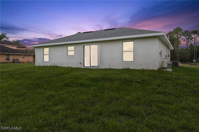 back house at dusk featuring central air condition unit and a yard