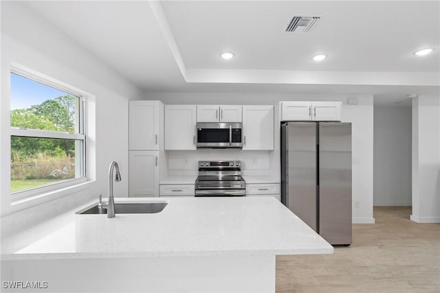 kitchen with stainless steel appliances, sink, white cabinets, light stone counters, and light wood-type flooring