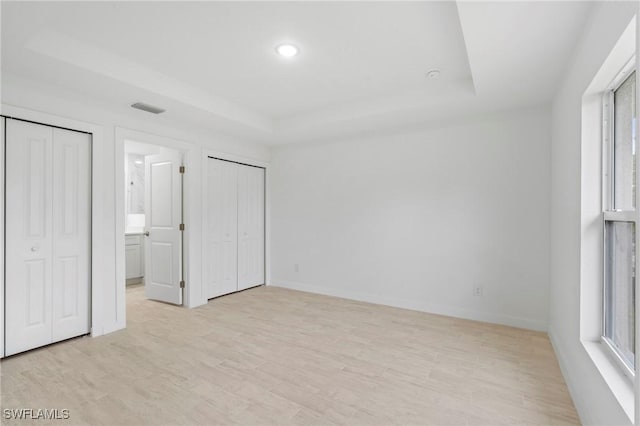 unfurnished bedroom featuring light wood-type flooring, connected bathroom, and a raised ceiling