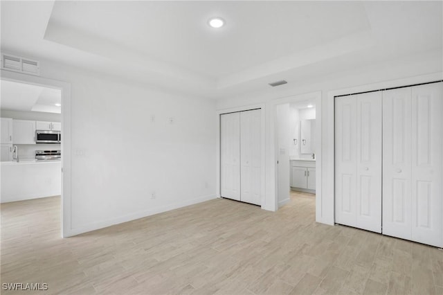 unfurnished bedroom featuring ensuite bath, a raised ceiling, light wood-type flooring, and sink