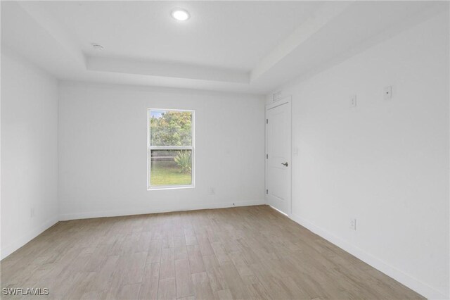 spare room with light wood-type flooring and a tray ceiling