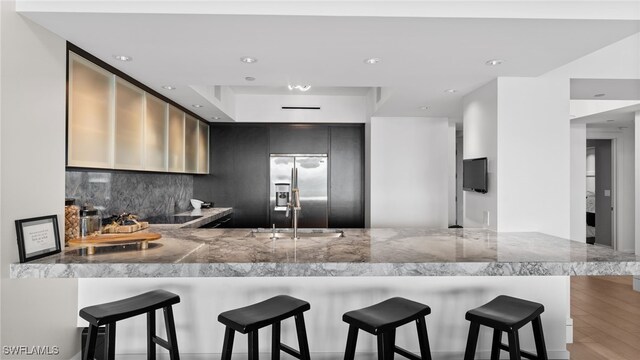 kitchen featuring sink, tasteful backsplash, stainless steel fridge with ice dispenser, kitchen peninsula, and a kitchen bar