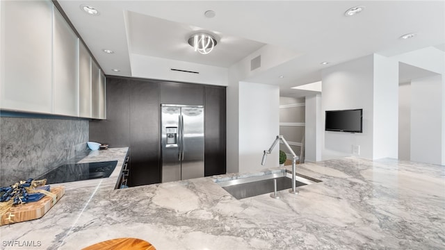 kitchen featuring tasteful backsplash, visible vents, light stone counters, stainless steel refrigerator with ice dispenser, and a sink