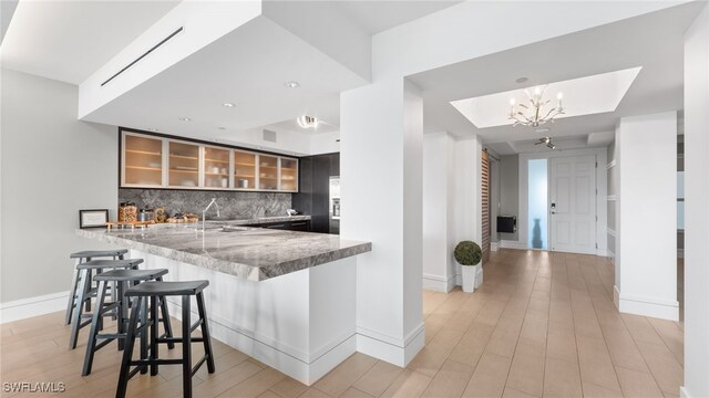 kitchen with backsplash, glass insert cabinets, a breakfast bar area, light wood-style floors, and a sink