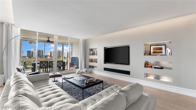 living room with a wall of windows, baseboards, wood finished floors, and ceiling fan