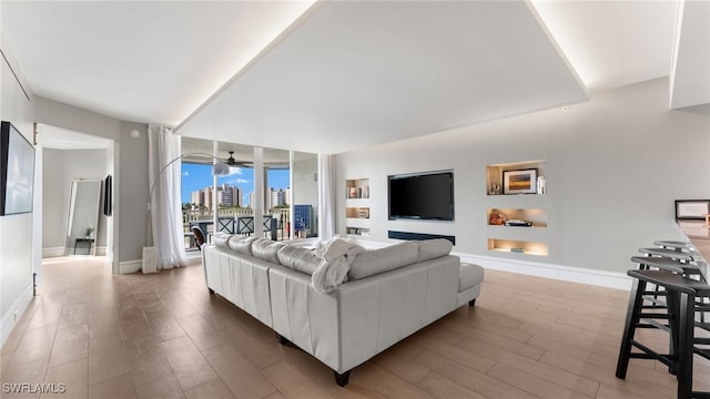 living room with a ceiling fan, wood finished floors, baseboards, and expansive windows